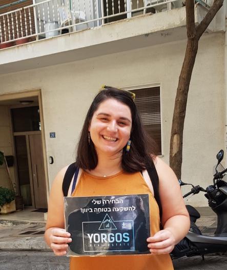 Happy client of Yorgos Real Estate company with big smile, holding the company logo after sucessfully selling their property.