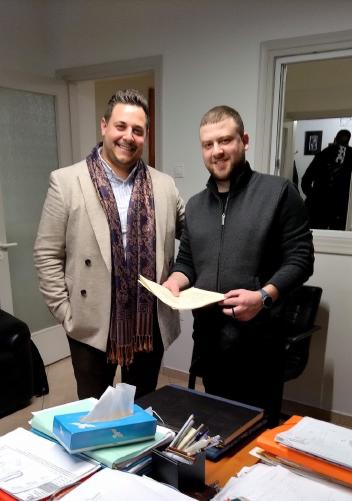 Happy client of Yorgos Real Estate company with big smile holding the documents of their newly purchased property, standing next to the company owner Mr. Yorgos.