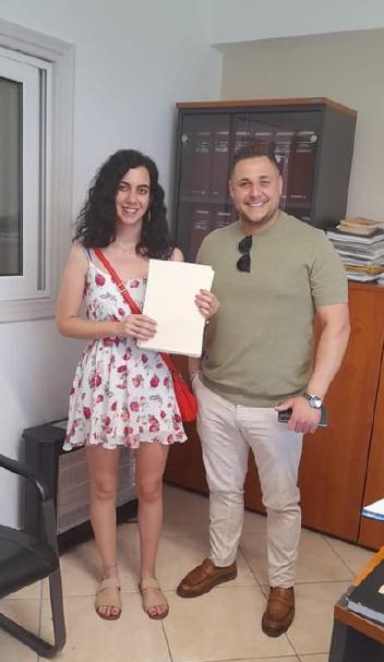 Happy client of Yorgos Real Estate company with big smile holding the documents of their newly purchased property, standing next to the company owner Mr. Yorgos.